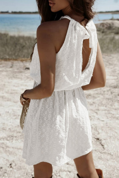 Robe mini blanche sans manches en dentelle avec nœud, taille nouée dans le dos et découpes.